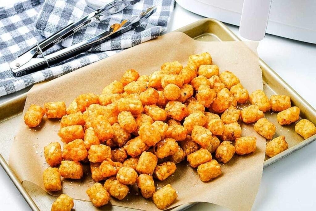 air fryer tater tots after cooking on baking sheet next to tongs