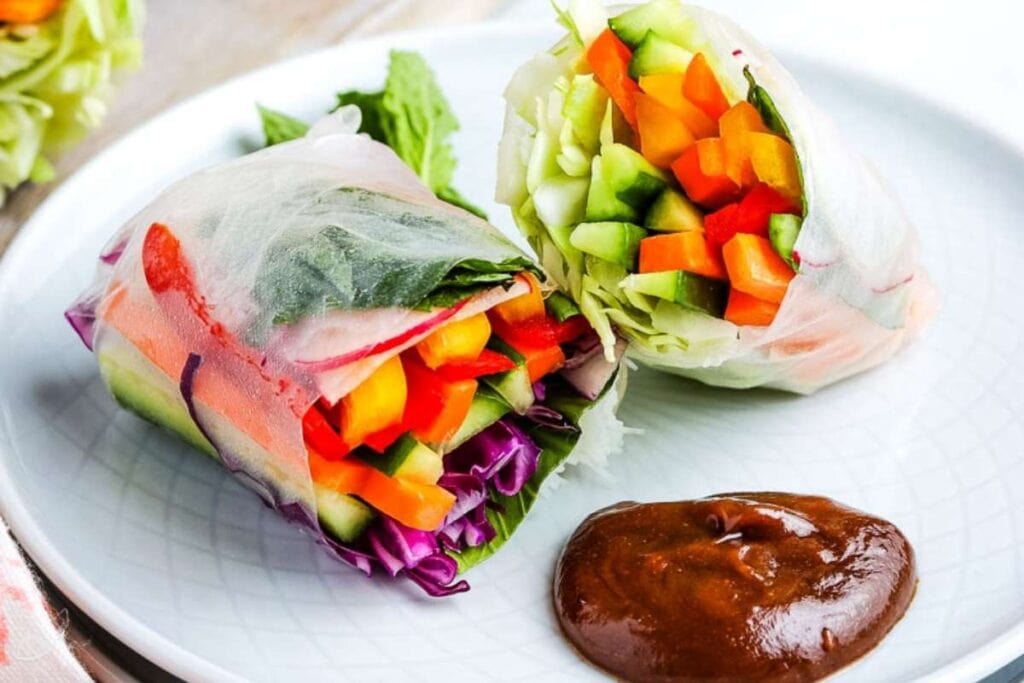 closeup of a summer roll on a white plate with homemade peanut sauce