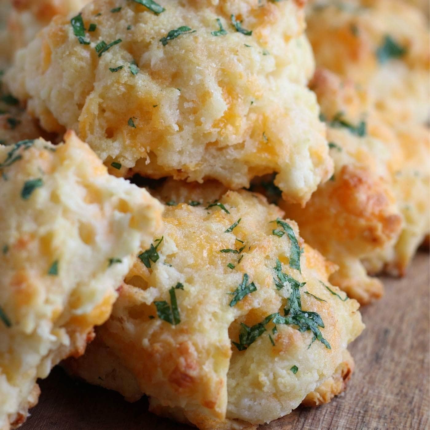 Closeup view of a Bisquick cheddar biscuits stacked on a wooden cutting board.