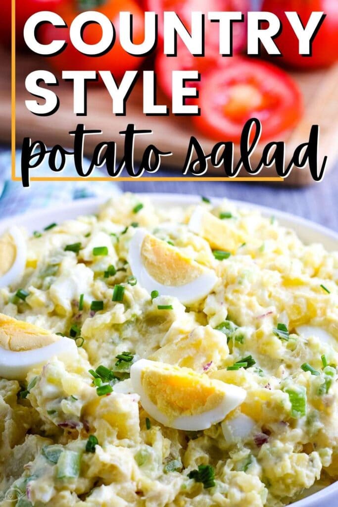 closeup view of a white bowl of country style potato salad with sliced tomatoes in the background and a graphic overlay