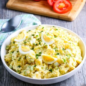 white bowl filled with country style potato salad on a wooden background with sliced tomatoes in the background