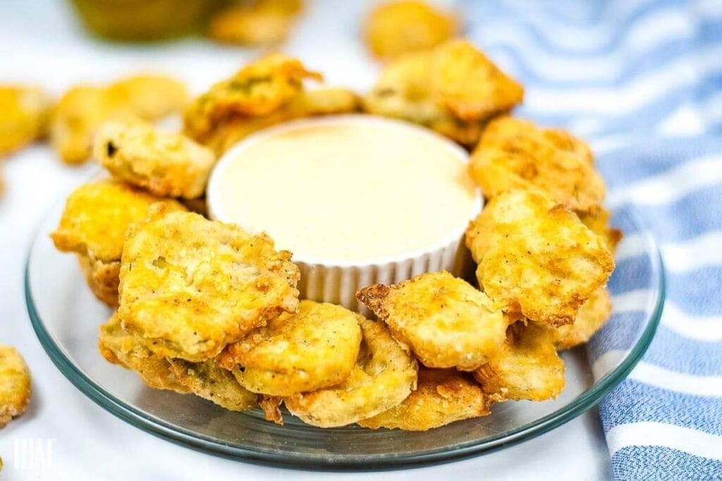 Air fryer pickle chips on a glass plate with a bowl of sauce in the middle.