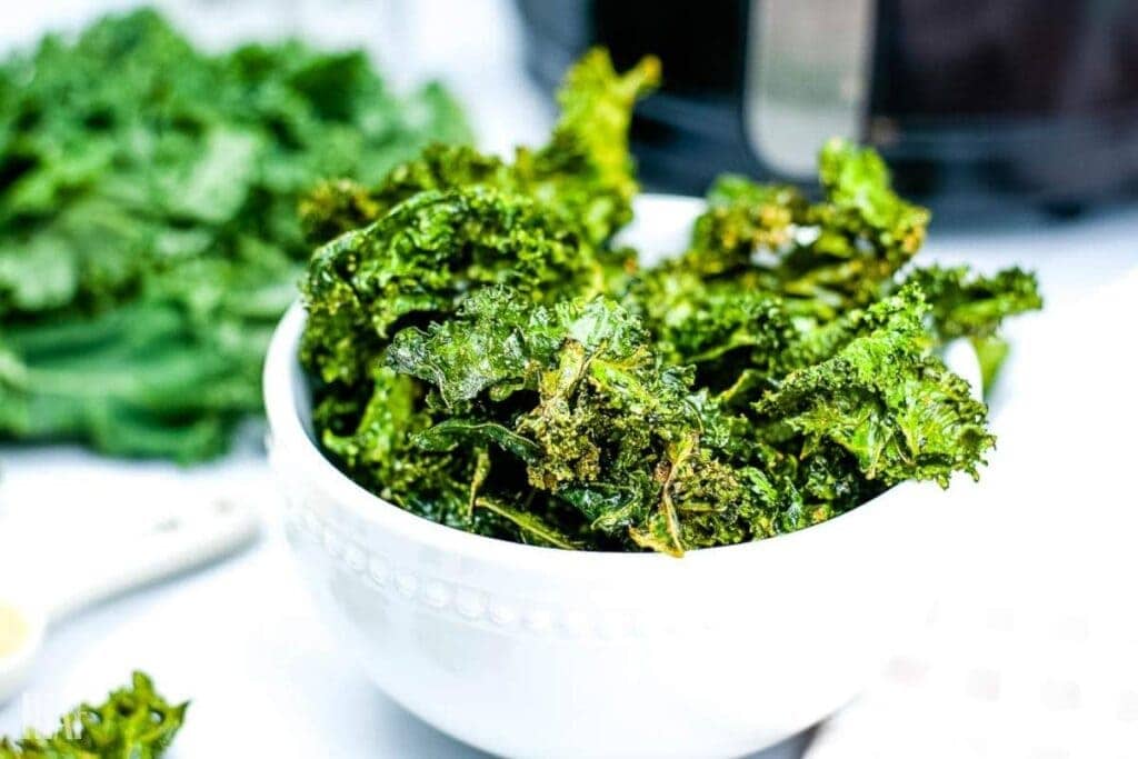 kale chips in a white bowl that was just cooked in the air fryer with more in the background