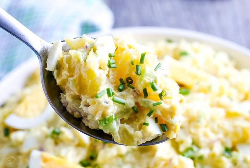 closeup of potato salad on a spoon garnished with chives