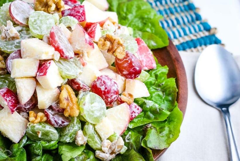 close up of waldorf salad in a brown bowl next to spoon