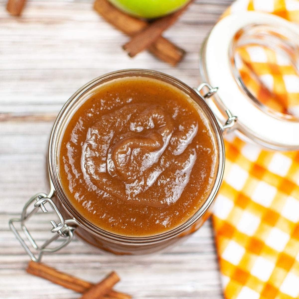 top shot of instant pot apple butter in a glass jar next to cinnamon sticks
