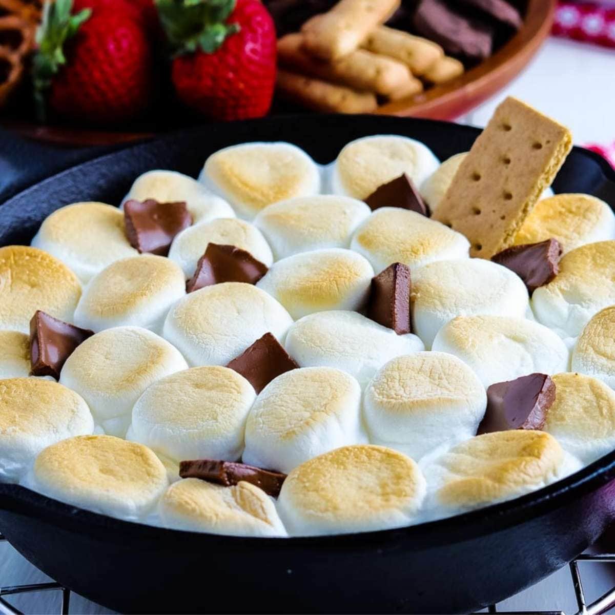 baked skillet smores dip garnished with a graham cracker and chocolate pieces
