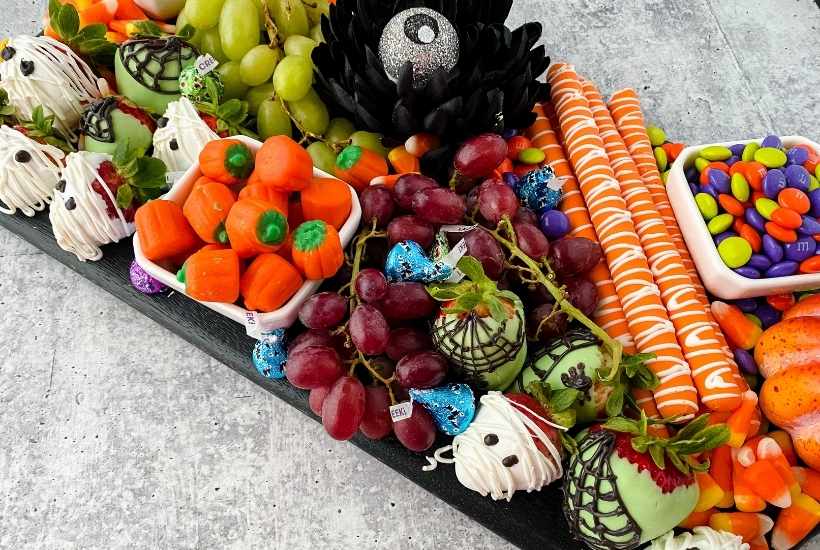 a halloween charcuterie board with chocolate covered strawberries, halloween candies, and decor