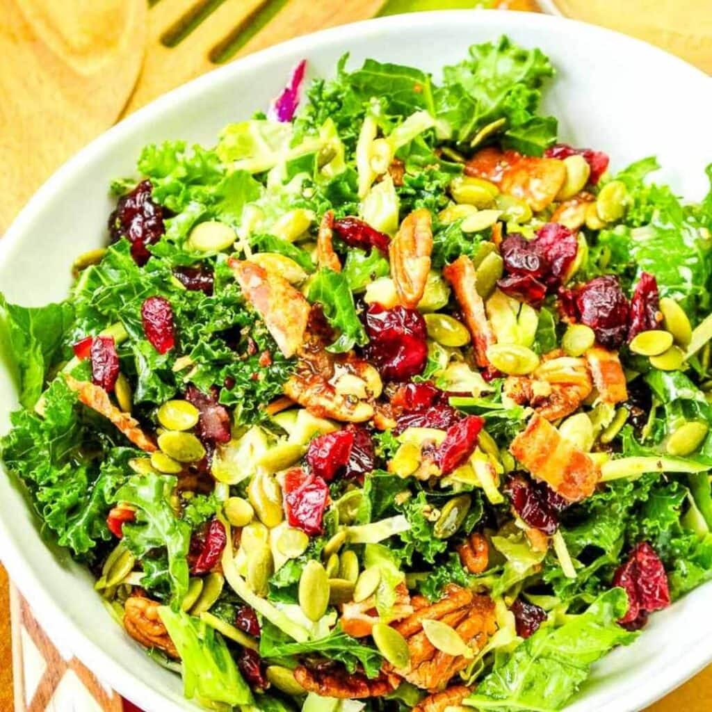 Kale and Brussel Sprout Salad with Cranberries with seeds and pecans in a white bowl