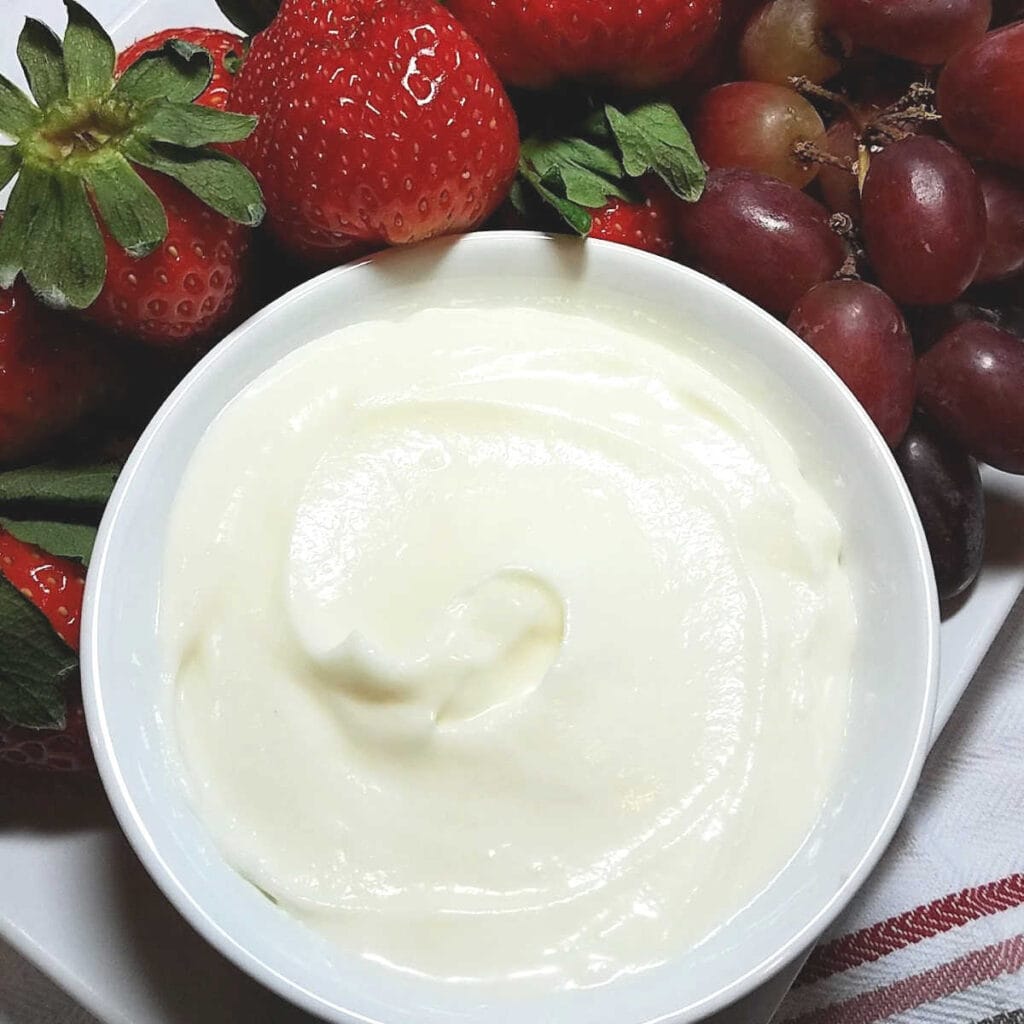 White bowl filled with fluffy fruit dip served with strawberries & grapes.