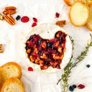 top shot of baked brie with walnuts and cranberries next to bread and nuts