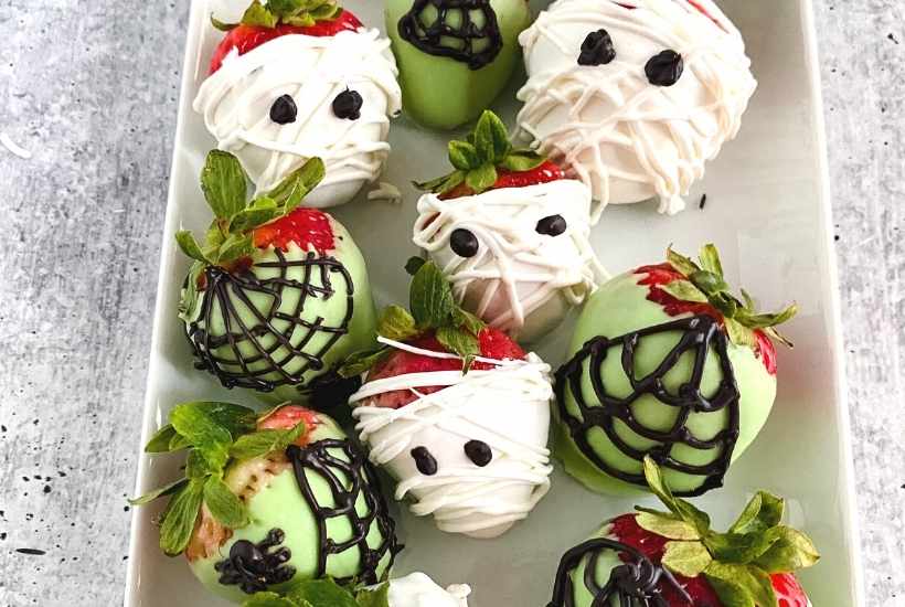 plate of halloween chocolate covered strawberries as mummies and spider webs with spiders