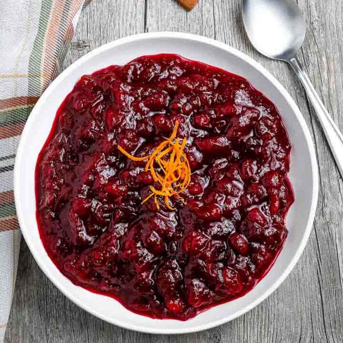 white bowl filled with homemade cranberry sauce on a grey wooden background with napkin and spoon