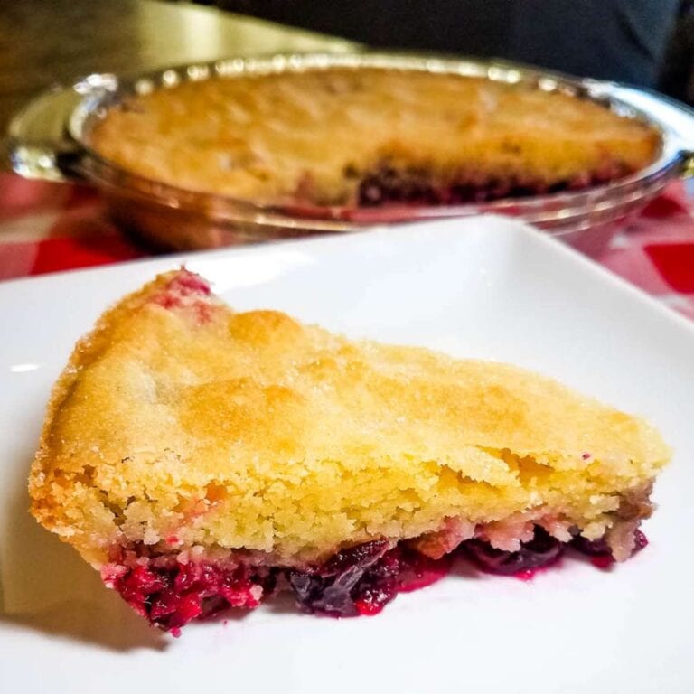 slice of Nantucket Cranberry Pie on a white plate with remainder of pie in the background