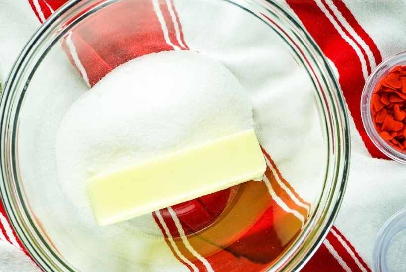 butter and sugar in a glass mixing bowl next to bowl of sprinkles