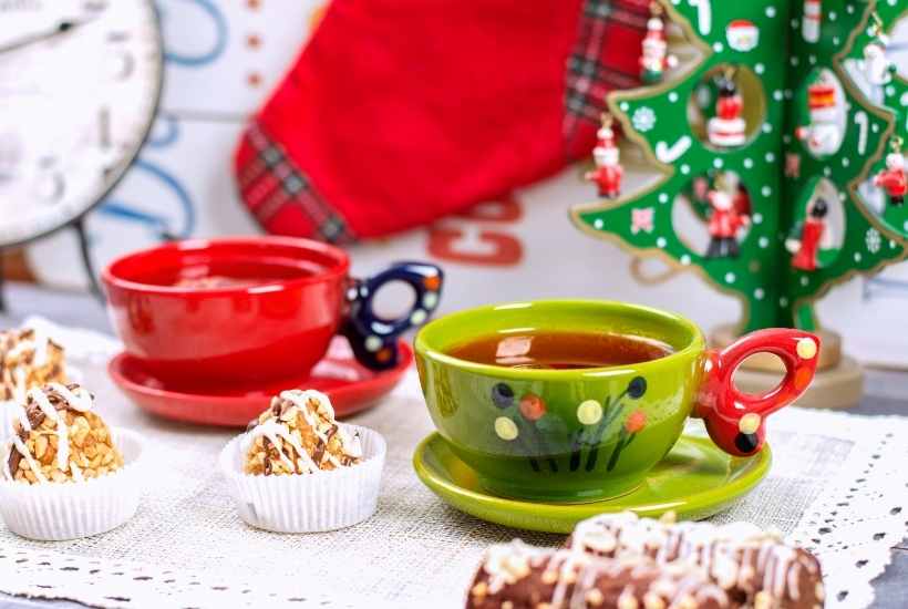 Christmas tea cups next to treats and a decorative Christmas tree.