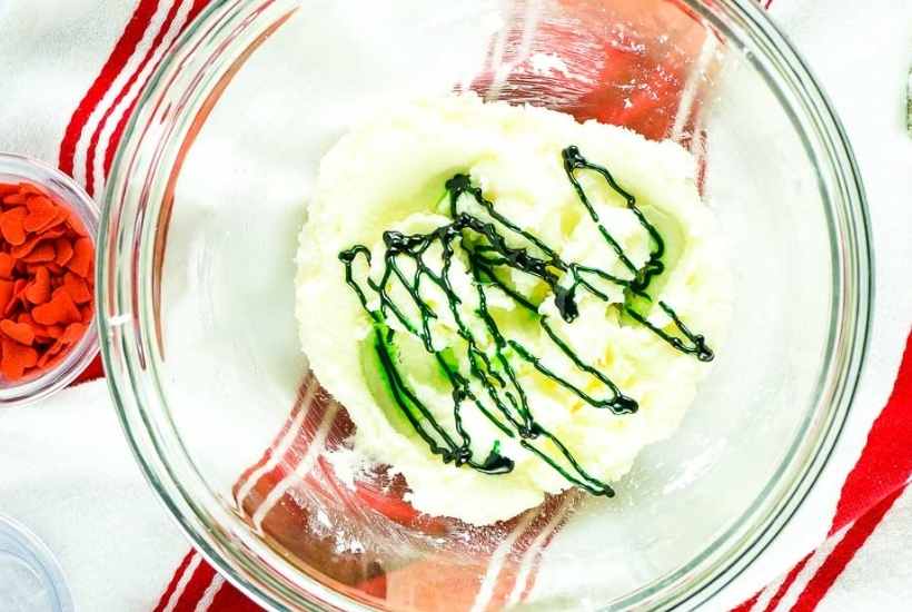 cookie dough in a mixing bowl drizzled with green food coloring