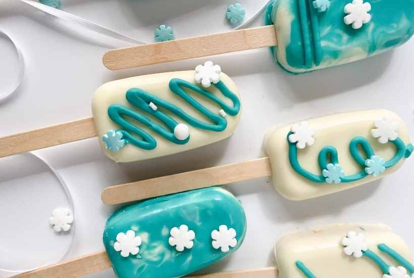 close up of Frozen themed  cakesicles with blue and white icing and snowflake sprinkles.