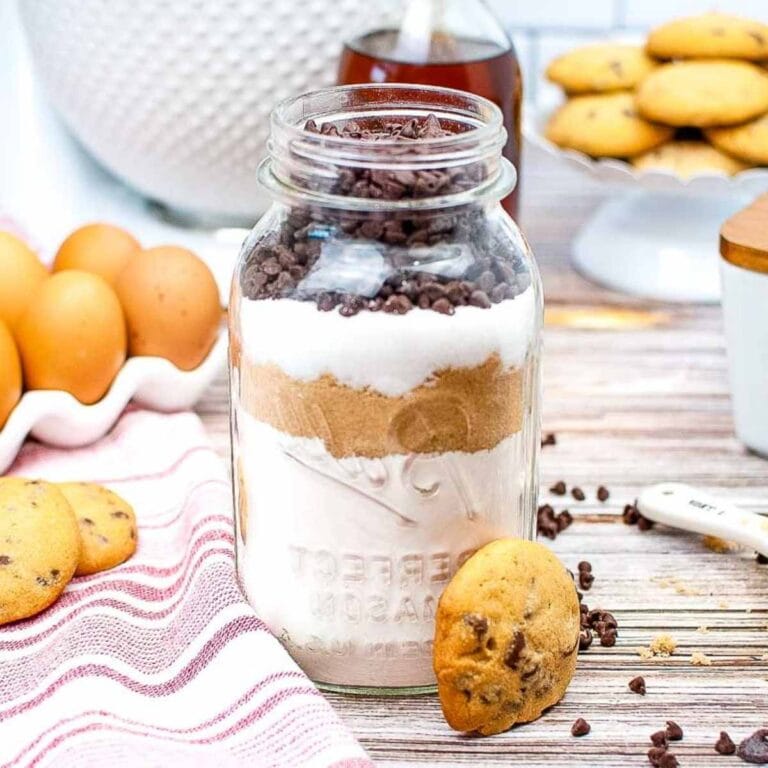 a mason jar with chocolate chip cookie mix inside next to baked cookies
