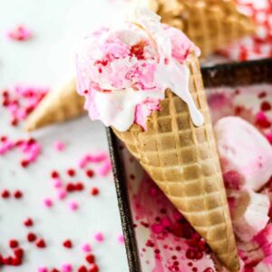 valentines day vanilla ice cream dripping down a waffle cone with sprinkles in the background