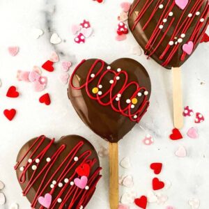 closeup view of three heart shaped cakesicles with sprinkles on a marble background