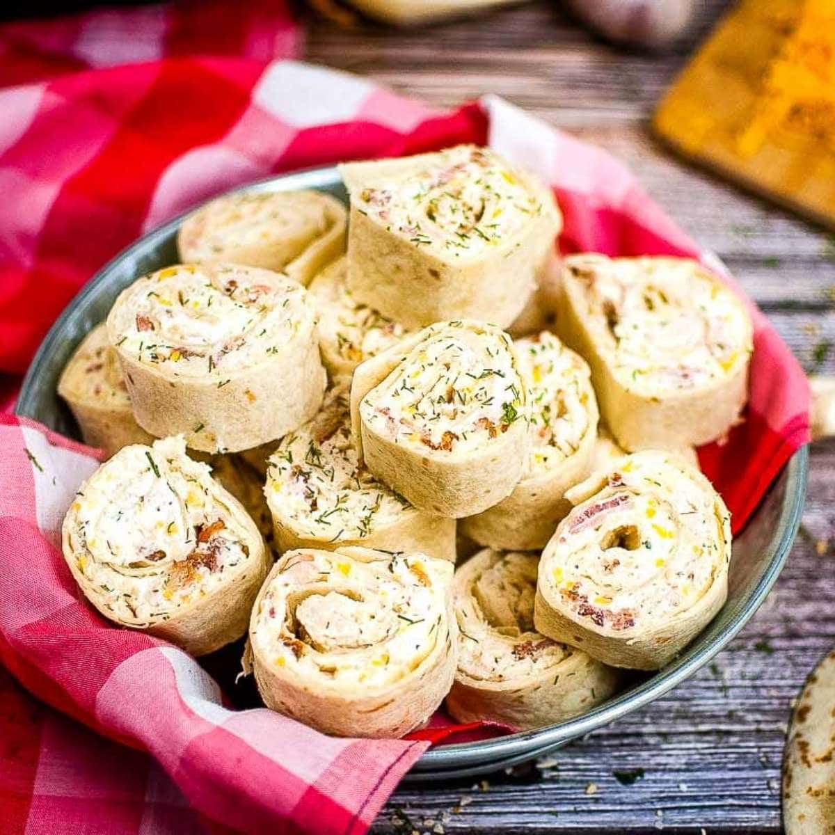 crack chicken pinwheels stacked in a pie plate with a red plaid dish cloth.