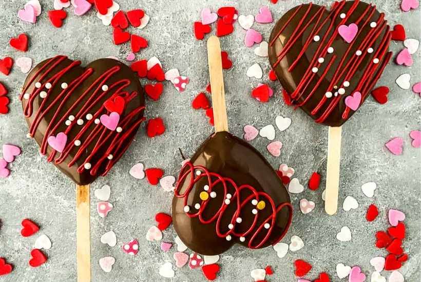 three strawberry heart cakesicles surrounded by sprinkles