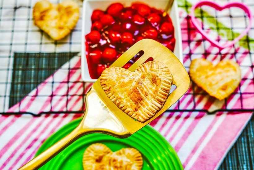 a baked heart shaped hand pie on a gold spatula with more pies in the background 