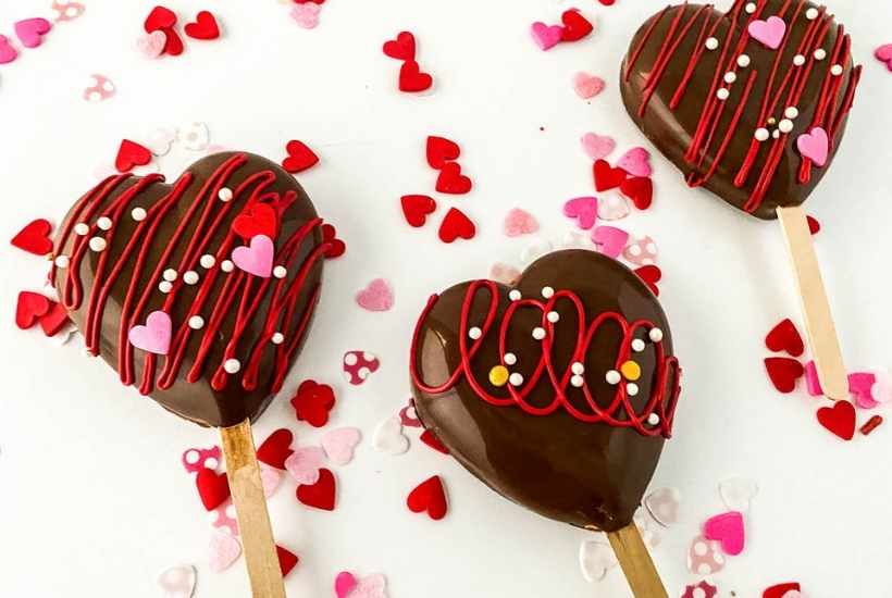 chocolate dipped heart cakesicles next to valentines sprinkles