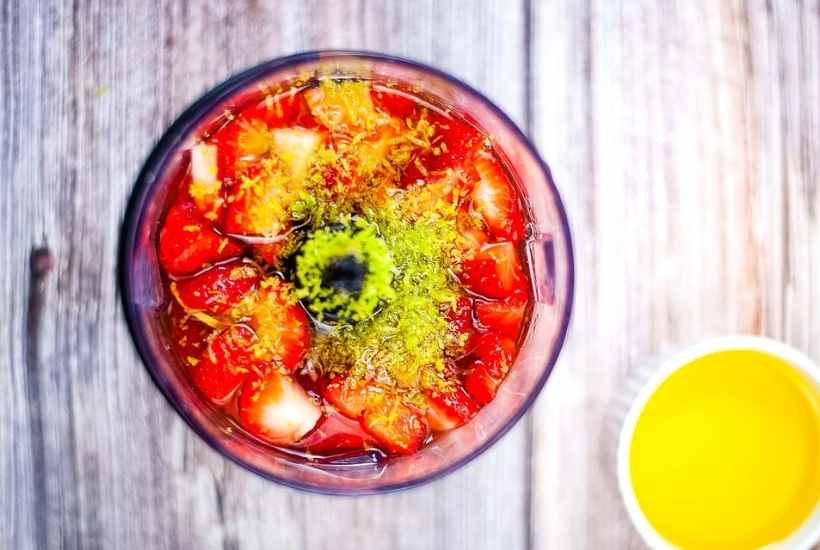 Overhead view of strawberry lime dressing ingredients in a blender next to a ramekin of oil.
