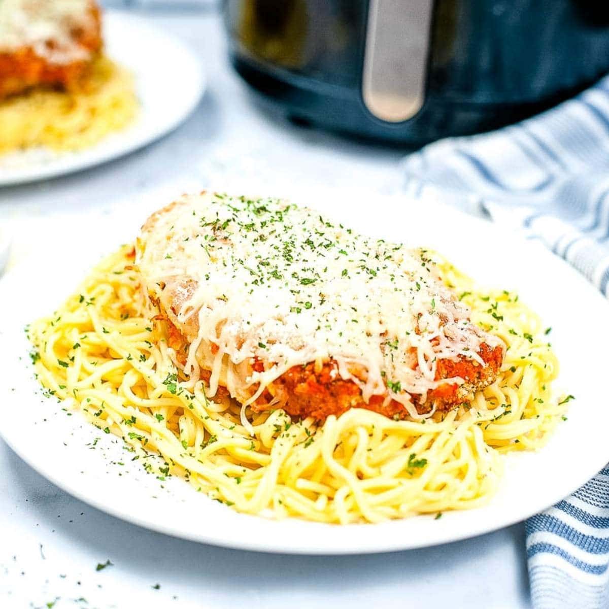 air fried chicken parmesan topped with mozzarella cheese on a bed of spaghetti on a white plate