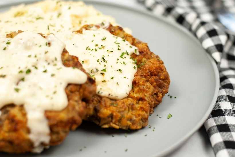 close up of air fryer chicken fried steak with gravy on top on a grey plate