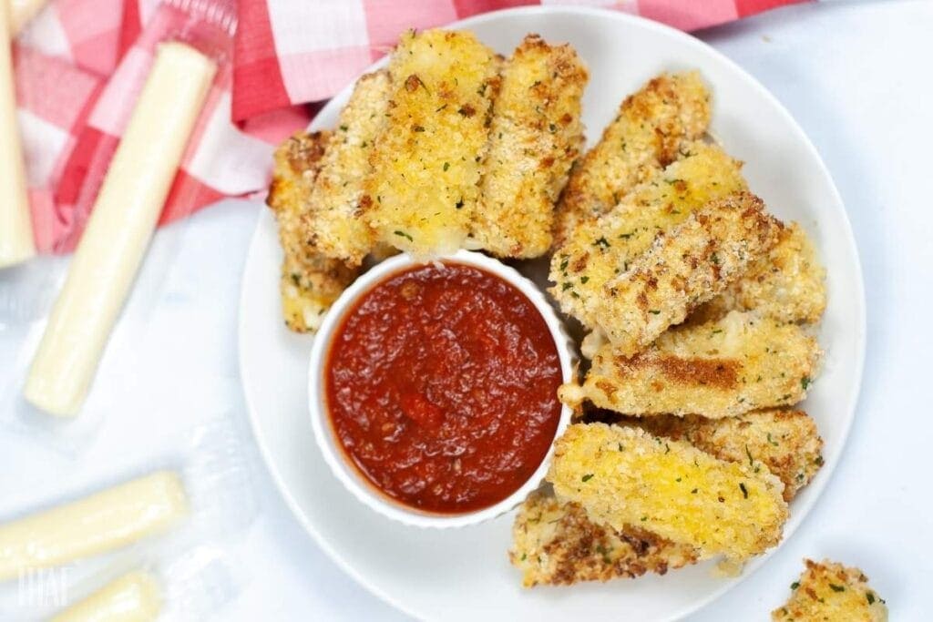 top shot of air fried mozzarella sticks on a white plate with a ramekin of marinara sauce