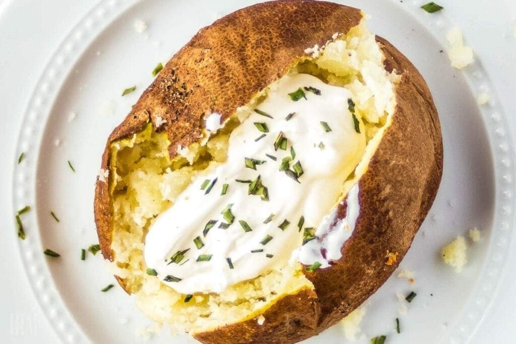 close up of baked potato with sour cream and chives on white plate