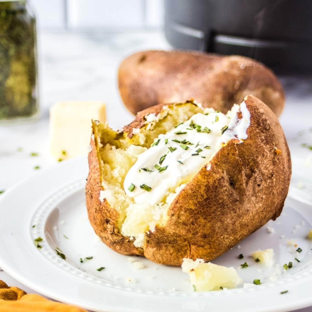 closeup of air fried baked potato garnished with sour cream & chives on a white plate