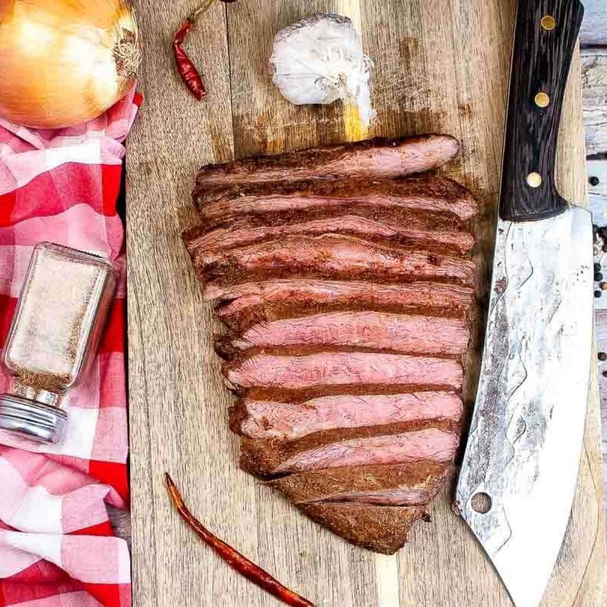 sliced air fried flank steak on a cutting board next to knife