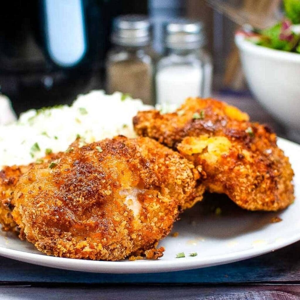 close up of 2 boneless chicken thighs made in the air fryer on a plate with a site of white rice