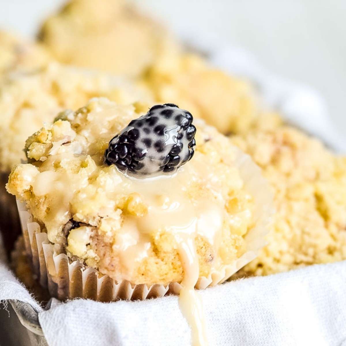 close up of blackberry lemon muffins topped with a whole blackberry and homemade glaze