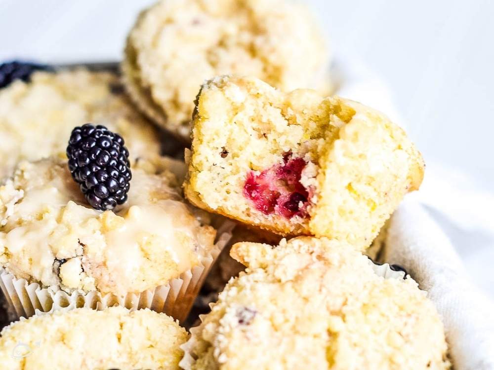 a batch of blackberry lemon muffins with a bite out of one