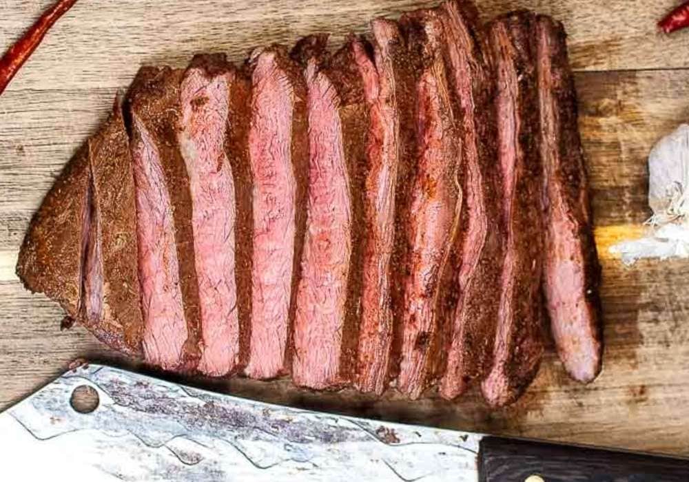 sliced flank steak next to a knife on a wooden cutting board