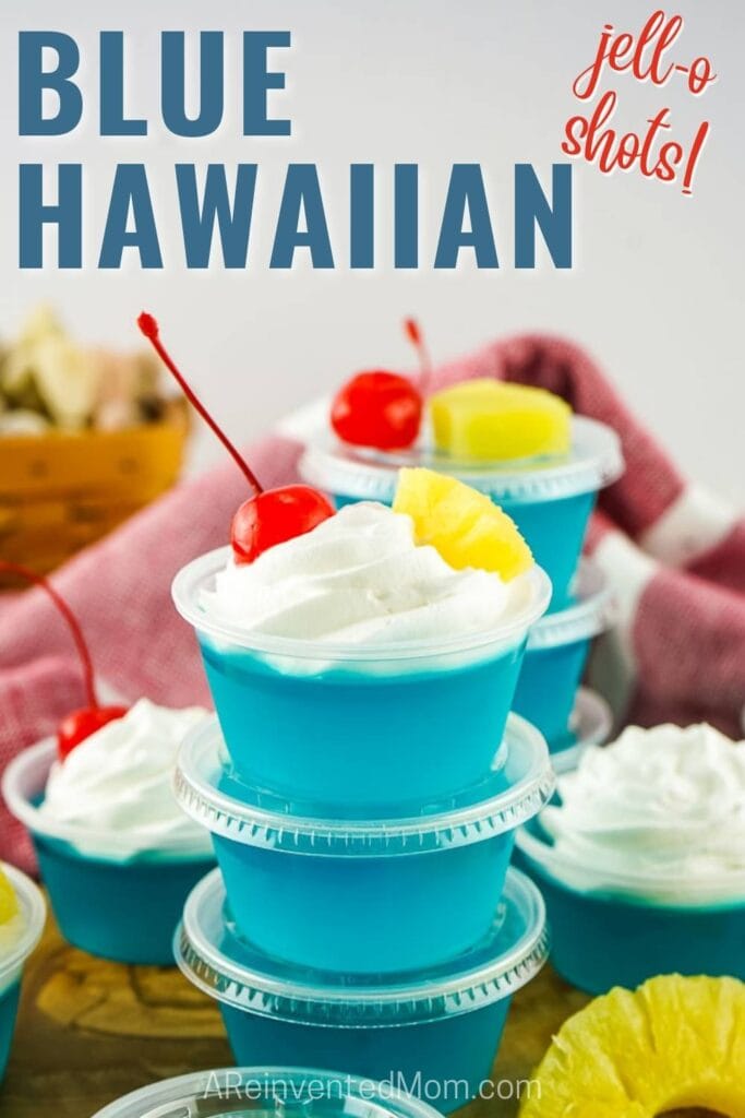 blue hawaiian jello shots stacked on top of each other with a whipped cream and fruit garnish and text overlay