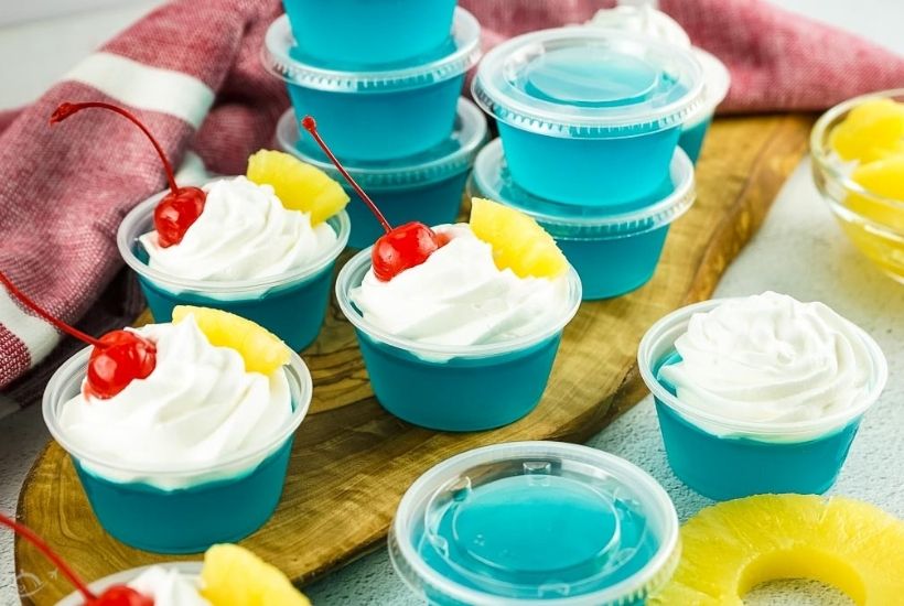 blue hawaiian pineapple Jello shots garnished with whipped cream, pineapple and cherries