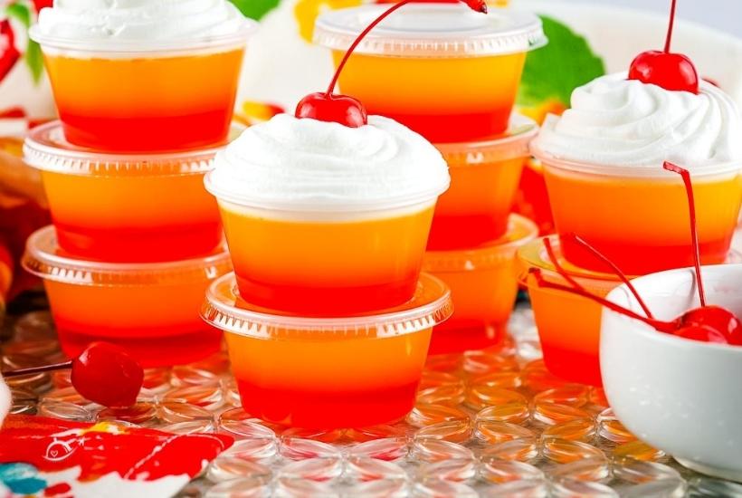 tequila sunrise jello shots stacked on top of each other some garnished with whipped cream and cherries