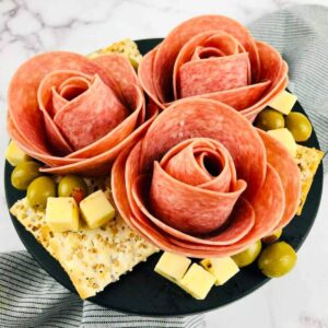 three salami roses on a serving tray with cheese, crackers, and olives