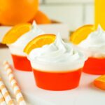 three mimosa jello shots with whipped cream and an orange slice for garnish