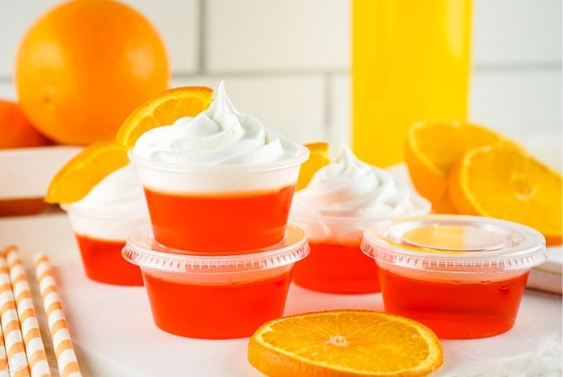 several mimosa jello shots with whipped cream next to oranges