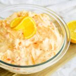 closeup of bowl of mandarin orange jello salad on a wooden cutting board