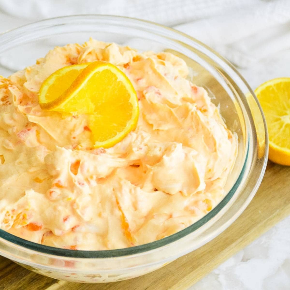 closeup of bowl of mandarin orange jello salad on a wooden cutting board