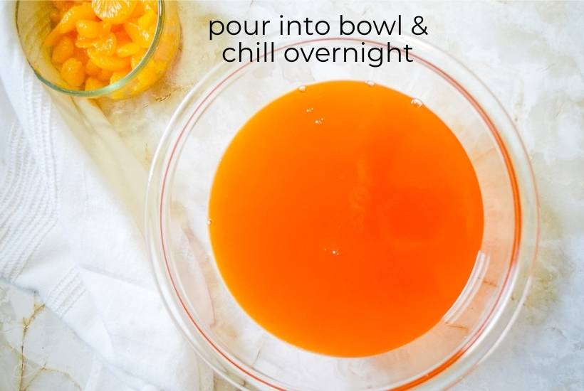 Cooked gelatin mixture in a clear bowl with a bowl of oranges in the background.