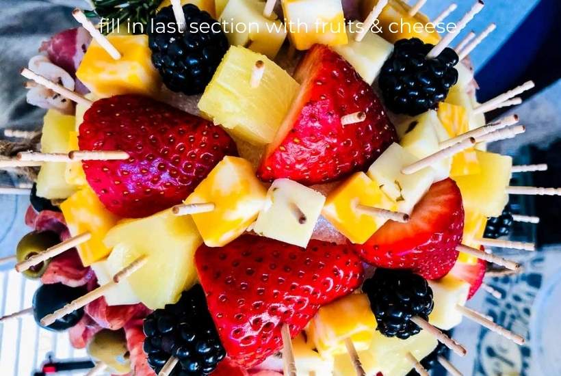 fruit and cheese being added to the charcuterie ball with toothpicks